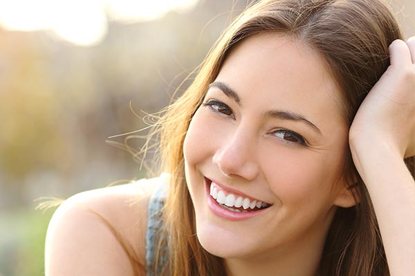 A smiling woman with long hair leaning on her hand, looking over her shoulder.