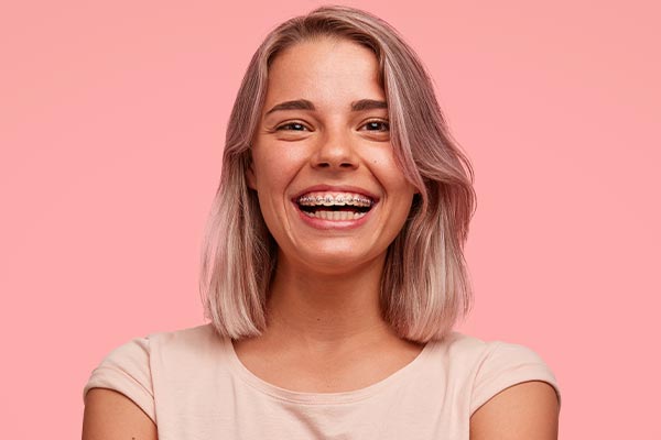 The image shows a smiling person with short hair, wearing a light-colored top against a pink background.