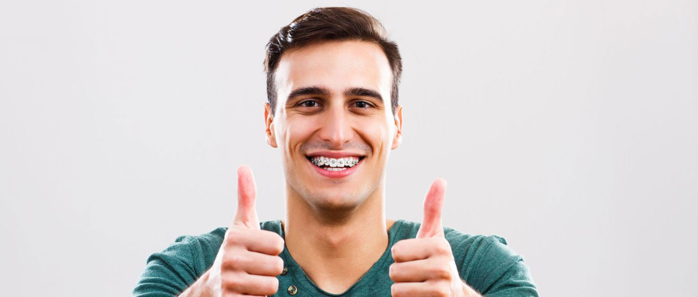 The image displays a man giving a thumbs-up with a smile, against a plain background.