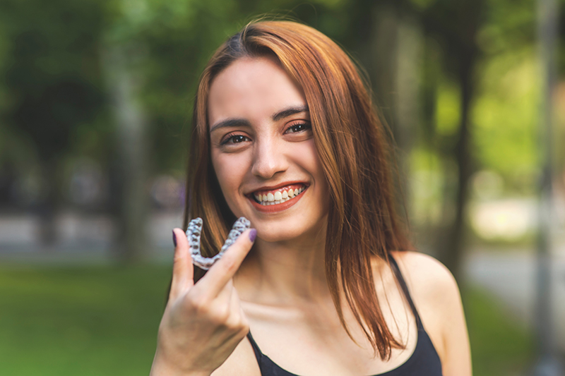 A woman with red hair smiles at the camera while holding up a ring on her finger.