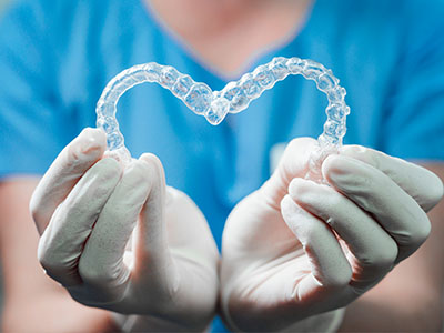 A person s hands are holding a heart-shaped object resembling dental braces, with a transparent background revealing a blue shirt and white gloves.