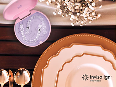 The image features a close-up view of a table setting with plates, cutlery, and a pink box containing what appears to be a dental impression kit, accompanied by a logo for Invisalign at the bottom right corner.