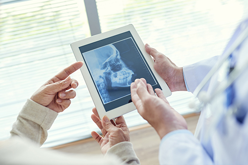 The image depicts two individuals engaged with a tablet displaying an X-ray, with a medical professional pointing at the screen while another person looks on.