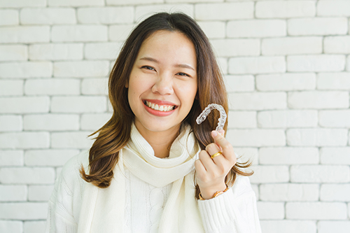 A smiling woman holding up a sign with a smiley face on it, standing in front of a brick wall.